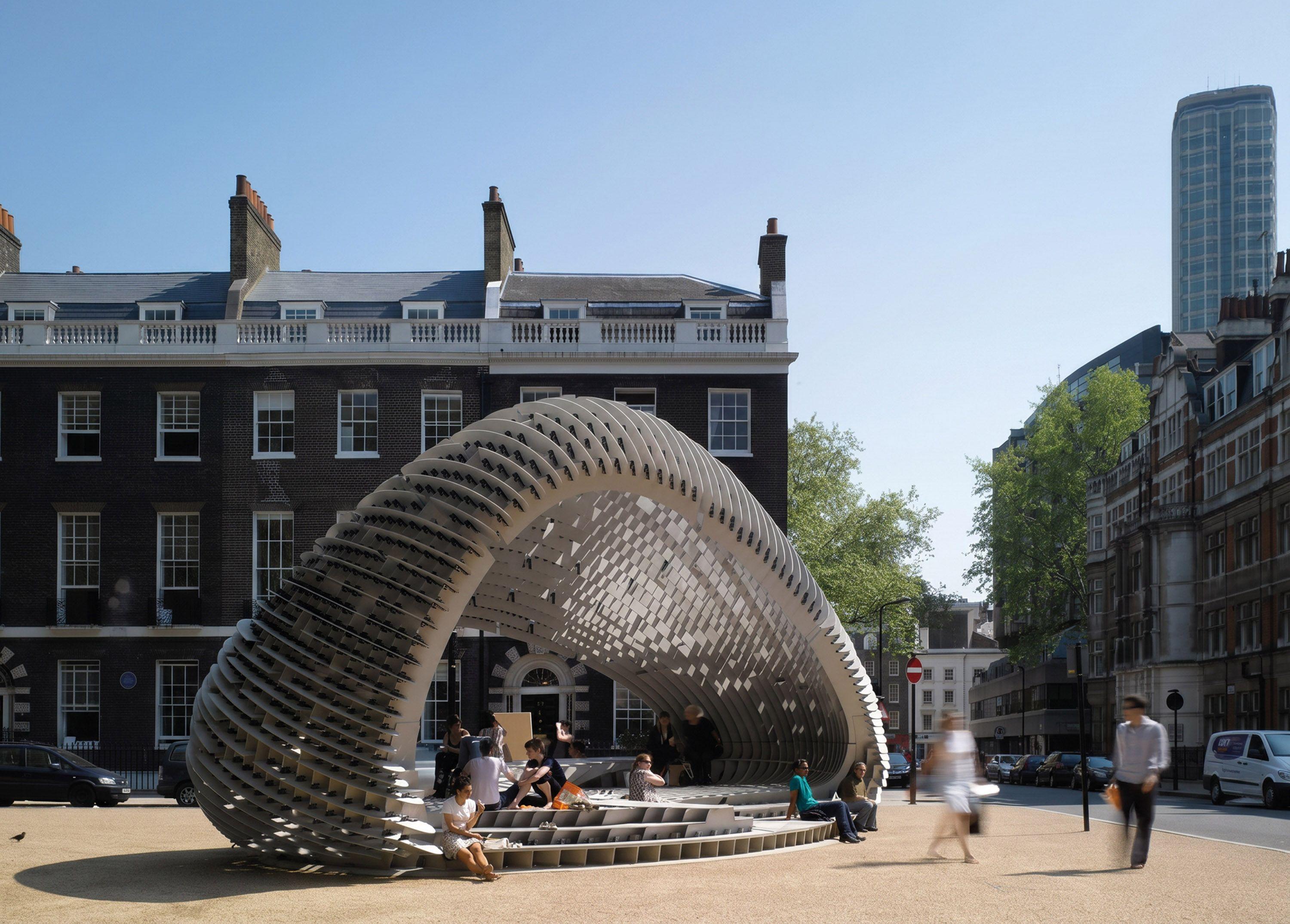 AA DRL Pavilion in Bedford Square, London, a curved lattice canopy of interlocking fins sheltering people seated on its stepped base.